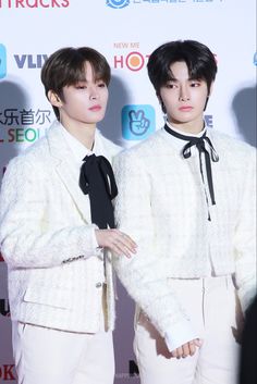 two young men in white suits standing next to each other on a red carpet with their hands behind their backs