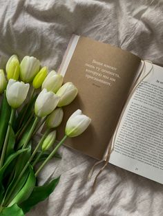 a bouquet of flowers sitting next to an open book on top of a white sheet