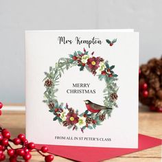 a christmas card with a bird on it and holly wreath in the middle, surrounded by pine cones