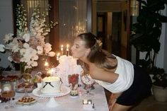 a woman blowing out candles on a cake at a table with flowers and other decorations