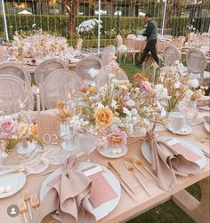 the table is set with pink and white plates, silverware, flowers and napkins