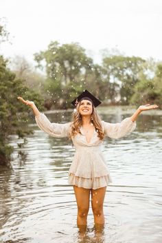 a woman standing in the water with her arms spread out and wearing a hat on top