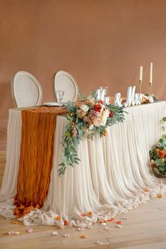 the table is set with white chairs and orange draping, along with flowers