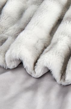 a white fur blanket is laying on top of a gray bed sheet with grey sheets