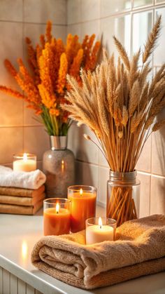 some candles are sitting on a table with towels and flowers in vases behind them