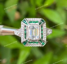 an emerald and diamond ring on top of a green plant