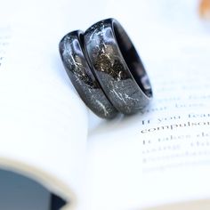 two wedding rings sitting on top of an open book with black and white marble inlays