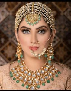 a woman wearing a gold and green bridal outfit with pearls on her head, nose ring