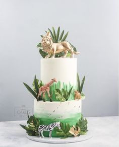 a three tiered cake decorated with jungle animals and plants, on a white table