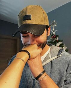 a man with a beard wearing a hat and looking at his cell phone while standing in front of a christmas tree