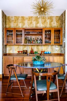 a dining room table with four chairs and a bar in the backround behind it