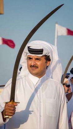 a man holding two large swords in front of other men wearing white outfits and hats