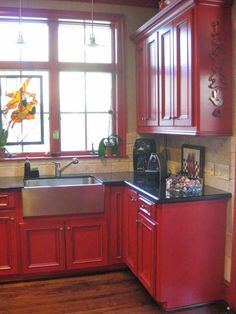 a kitchen with red cabinets and black counter tops in front of a window that is open to the outside