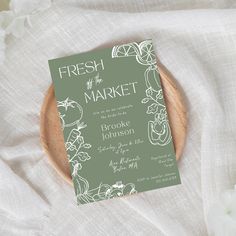 a green and white wedding card sitting on top of a wooden plate next to flowers