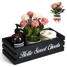 a black tray with flowers and soaps in it next to a white vase filled with pink carnations