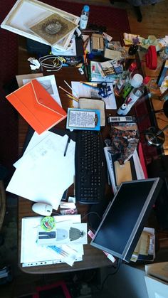 a cluttered desk with an open laptop and many other things on it, including papers