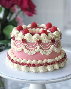 a pink and white cake with raspberries on top is sitting on a plate