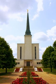 a large white building with a steeple and flowers in the foreground on a sunny day