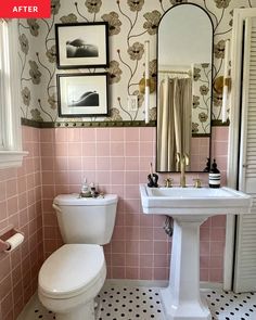 a white toilet sitting next to a sink in a bathroom under a mirror and framed pictures on the wall