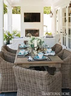 an outdoor dining area with wicker chairs and table set for four, in front of a fireplace