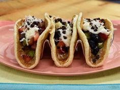 three tacos are sitting on a pink plate with white sauce and black beans in them