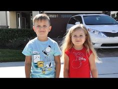 two young children standing next to each other in front of a house with cars behind them