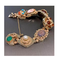 "14 karat yellow gold hollow vintage slide style charm bracelet.  This bracelet has turquoise, coral, amethyst, garnet, chalcedony, pearl, and green agate gemstones.  It measure approximently 8\" long and closes with a hidden box clasp and features a safety chain for extra security.  This bracelet is vintage in excellent condition, it has slight dents on the back of a couple charms.  This bracelet is truely a unique stunner!!" Heirloom Gold Multi-stone Bracelets, Heirloom Gold Bracelets With Multi-stone, Fine Jewelry Bracelet With Cabochon, Vintage Oval Multi-stone Bracelets, Antique Multi-stone Bracelet As Gift, Antique Multi-stone Bracelets As Gift, Heirloom Yellow Gold Multi-stone Bracelets, Multicolor Fine Jewelry Collectible, Gold Cabochon Bracelet In Fine Jewelry Style