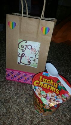 a paper bag with lucky charms on it next to a bowl of cereal and spoon