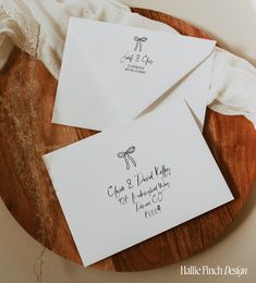 some white envelopes with writing on them sitting on a wooden plate next to a napkin