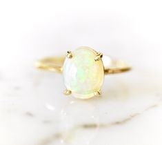 A 1-carat 8x6mm oval cabochon rainbow opal glows within a delicate 14-karat yellow gold setting. Romantic and timeless, contemporary yet feminine.  This opal is vibrant in color and these pictures just don't do it justice.  The colors are very intense ranging from red to green depending on the angle and the light source. natural Ethiopian  Opal  1.15-carat Oval Cabochon, 8 x 6 mm Natural Color - Yellow milky with speaks of rainbow hues.  Naturally included - Opaque, colors vary Each Opal is carefully hand-selected for its beauty.  Some have more inclusions than others but each will be beautiful! ❤︎ solid 14 Karat yellow gold  ❤︎Ready to ship in yellow gold Size 4.5 - Sizing available, message us for sizing. Select your ring size from the drop-down menu (Please note that larger sizes have a Yellow Gold Ethiopian Opal Oval Cabochon Ring, Yellow Gold Ethiopian Opal Ring In Oval Cabochon Shape, Yellow Gold Ethiopian Opal Ring In Oval Shape, Ethiopian Opal Oval Cabochon Ring In Yellow Gold, Yellow Gold Oval Solitaire Opal Ring, Oval Solitaire Opal Ring In Yellow Gold, Elegant Ethiopian Opal Ring In Oval Cabochon, Elegant Ethiopian Opal Ring, Oval Cabochon, Elegant Ethiopian Opal Ring Oval Cabochon