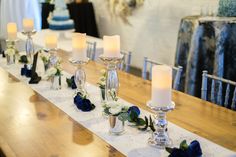 candles are lined up on a long table with blue flowers and greenery around them