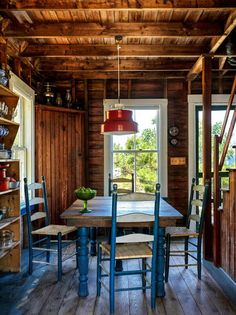 a table and chairs in a room with wooden walls, wood flooring and open windows