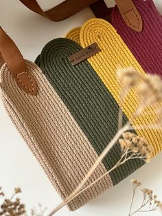 three different colored bags sitting next to each other on top of a white table with dried flowers