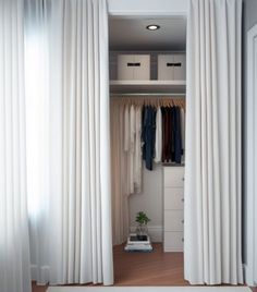 an open closet with white curtains and clothes on hangers