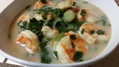 a white bowl filled with soup and vegetables on top of a table next to a napkin