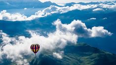 a hot air balloon flying high in the sky above some clouds and mountain range below