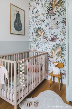 a baby crib in front of a wall with flowers and deers on it