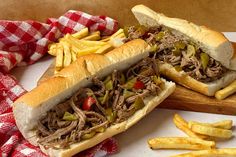 two sandwiches with meat, peppers and french fries on a cutting board next to a red and white checkered napkin