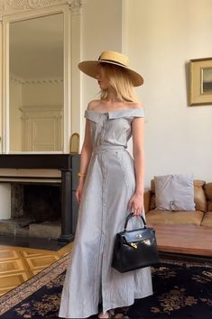 a woman in a dress and hat is holding a handbag while standing on a rug