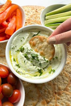 a person dipping dip in a bowl with vegetables and crackers on the side,