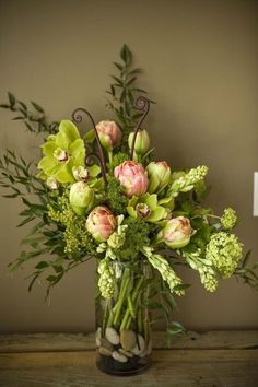 a vase filled with lots of flowers on top of a wooden table next to a wall