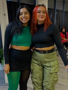 two women standing next to each other wearing green pants and black tops with their arms around each other