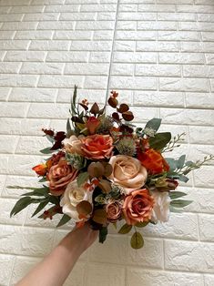 a hand holding a bouquet of flowers against a white brick wall