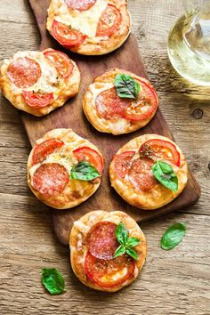 mini pizzas with tomatoes and basil on a cutting board next to some green leaves