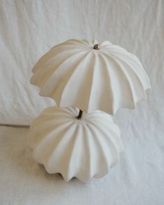 two white vases sitting next to each other on a white tablecloth covered surface