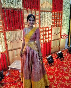 a woman in a yellow and pink sari standing next to a wall with red flowers