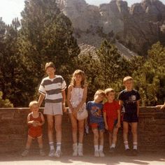 a group of young children standing next to each other in front of trees and mountains