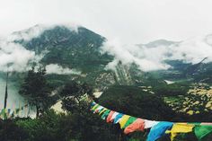 there are many colorful flags hanging from the clothes line in front of mountains and water