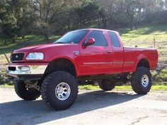 a red pick up truck parked in a parking lot next to some grass and trees