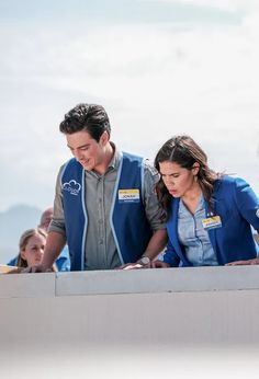 a man and woman standing next to each other in front of a wall looking at something